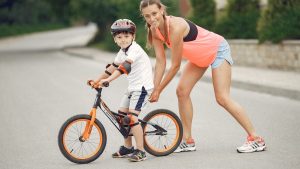 Mother helping her son ride a bicycle in a sunny outdoor setting. Bonding and learning experience.