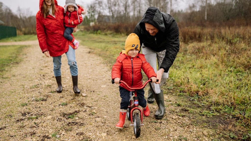 Happy family walking outdoors in fall, teaching child to ride bike.